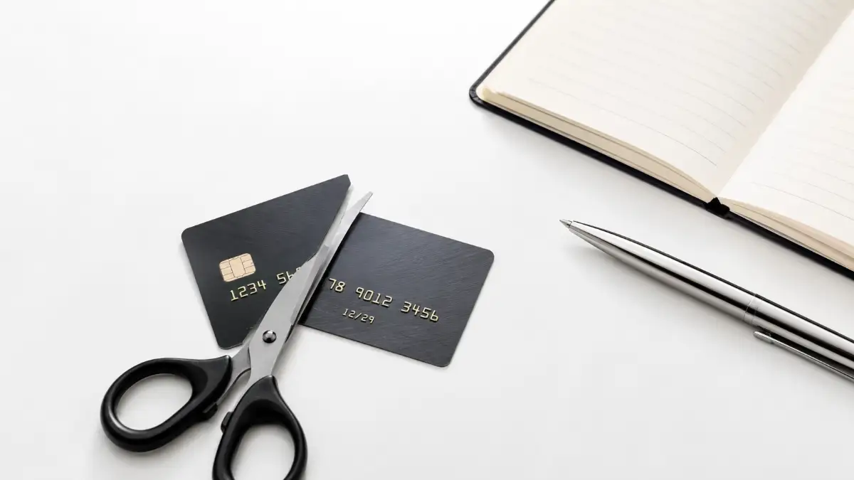 A premium credit card cut in half next to a notebook on a bright desk, representing the first step in learning the common mistakes to avoid when paying off credit card debt.